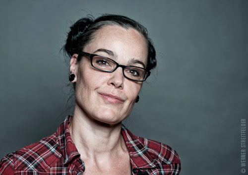 Farbportrait von Sunla Mahn mit Brille, keck in die Kamera lächelnd
